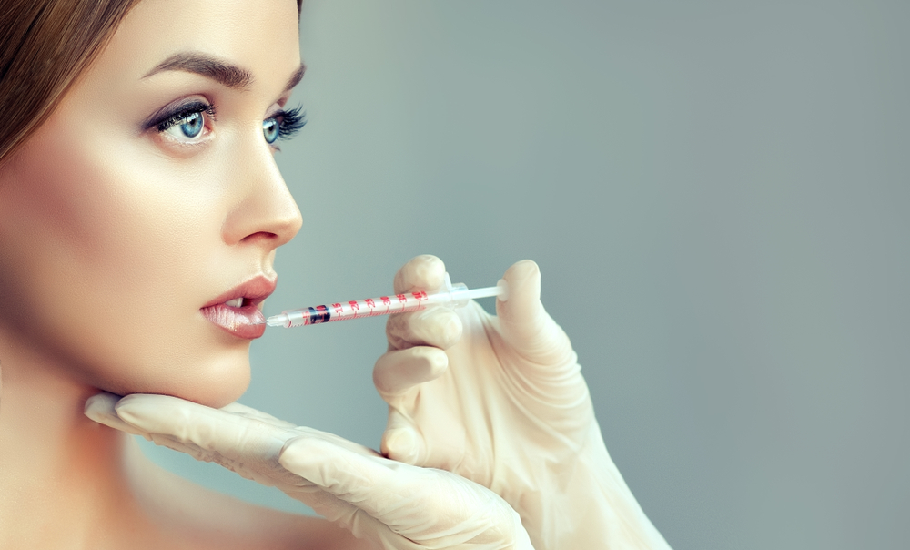 womans face receiving lip injection from needle with pair of gloved hands