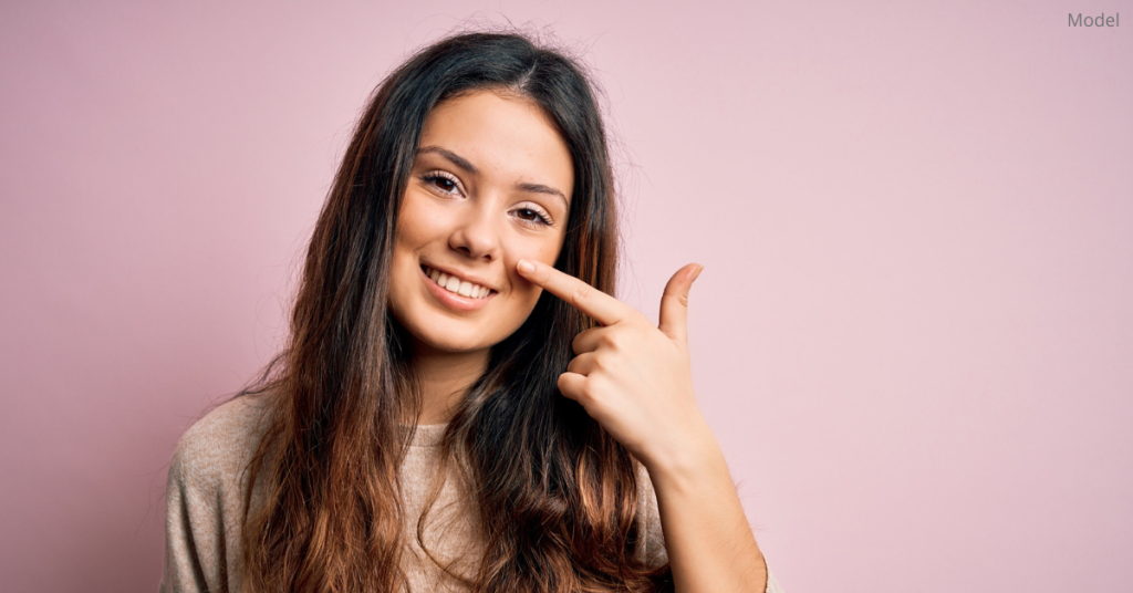 Woman (model) points to her nose while smiling.