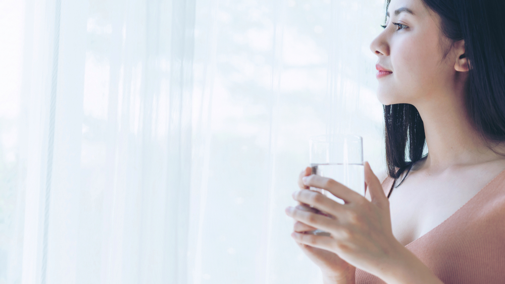Model looking out the window holding a glass of water