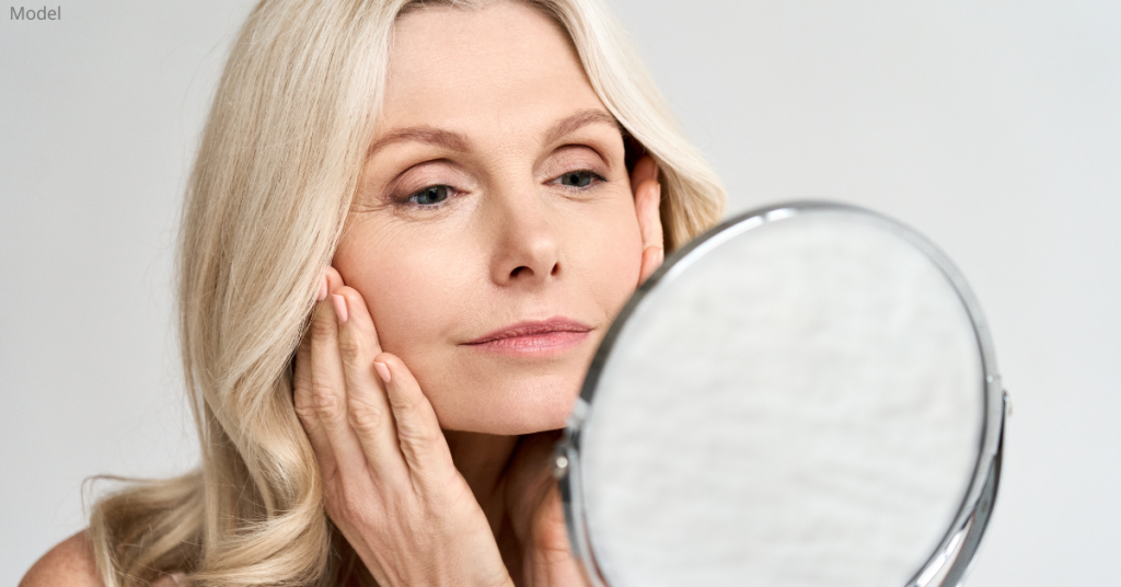 An older woman looking in the mirror and considering a facelift (model)