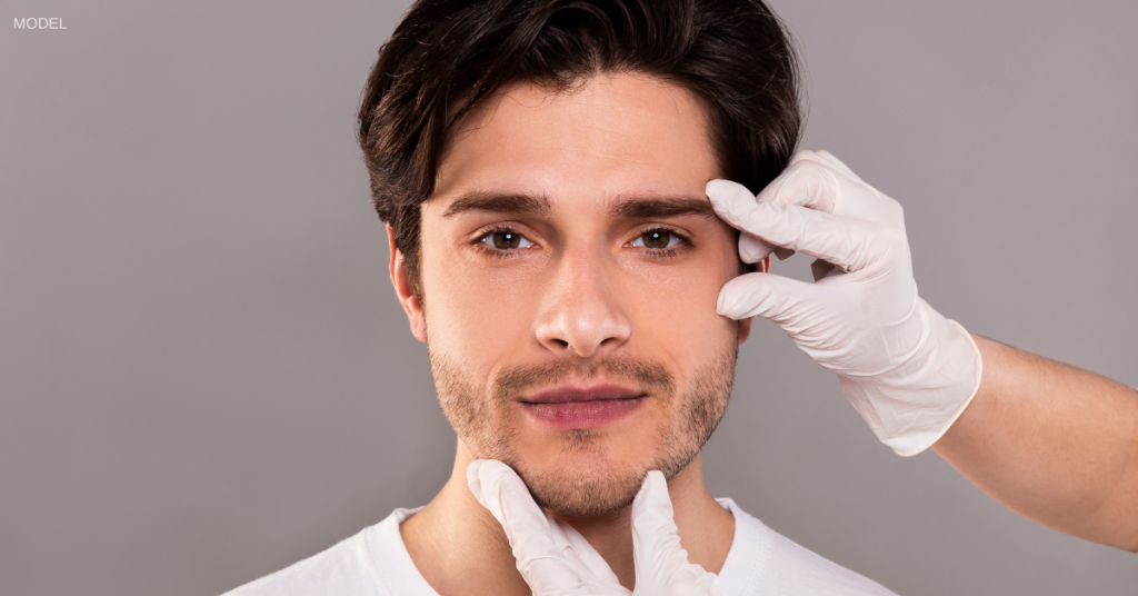 Man (model) having his face examined by a pair of gloved hands.