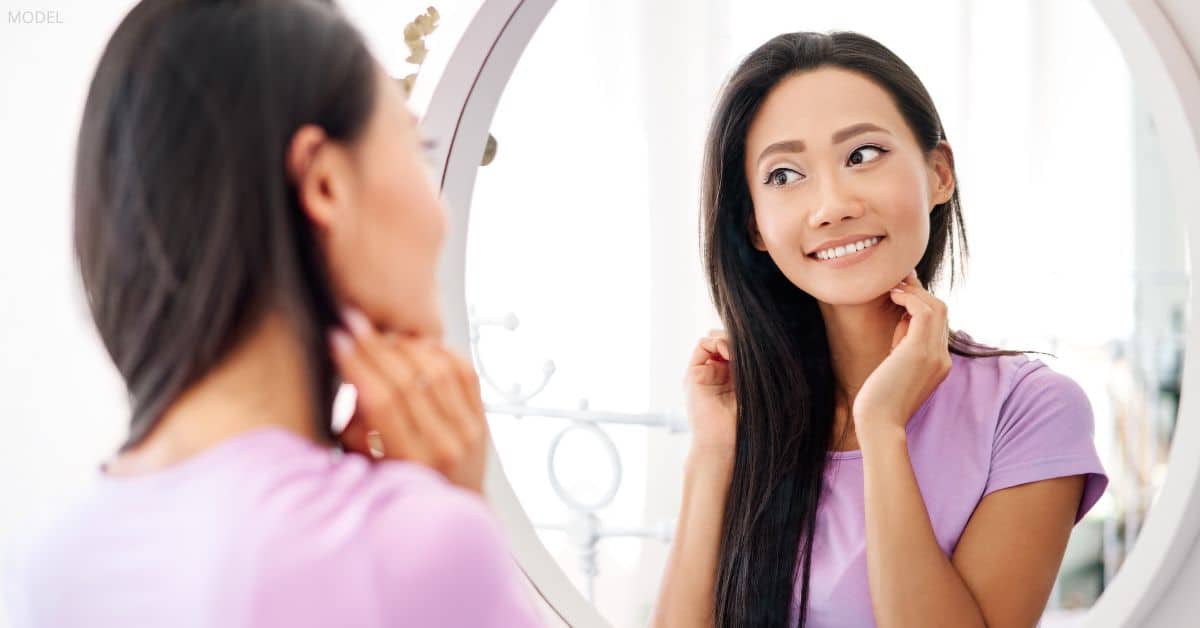 A woman (model) looking in the mirror in the bathroom.