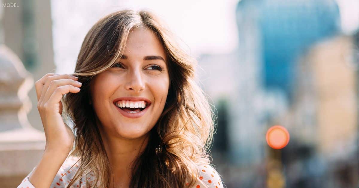 Woman (model) smiles while running a hand through her hair.