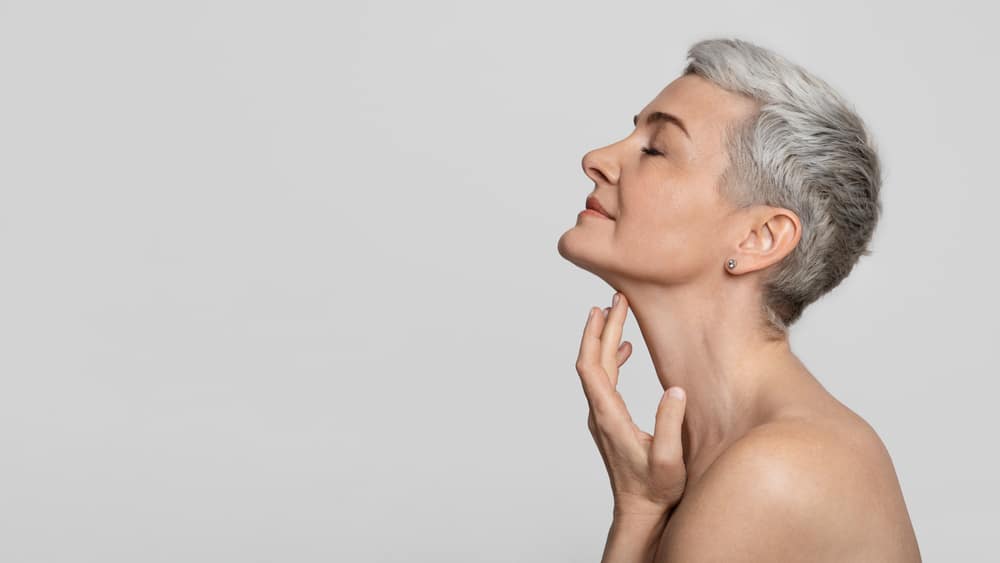 Side profile of an older woman touching her defined neck and jawline after getting neck liposuction.