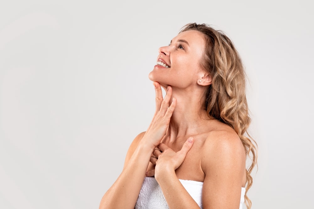 Beautiful woman looking up and touching her sharp, defined jawline after getting defining facial surgery.